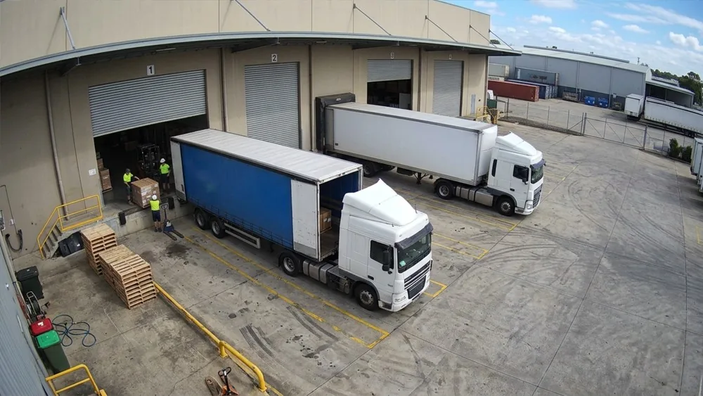 Eine Kamera an der Laderampe: zwei Lkw an den Toren, Paletten auf der Vorfläche